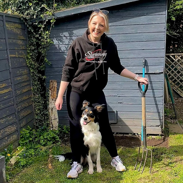 Slimming World Consultant Katie holding a digging fork in her garden. Her dog is sitting between her legs.