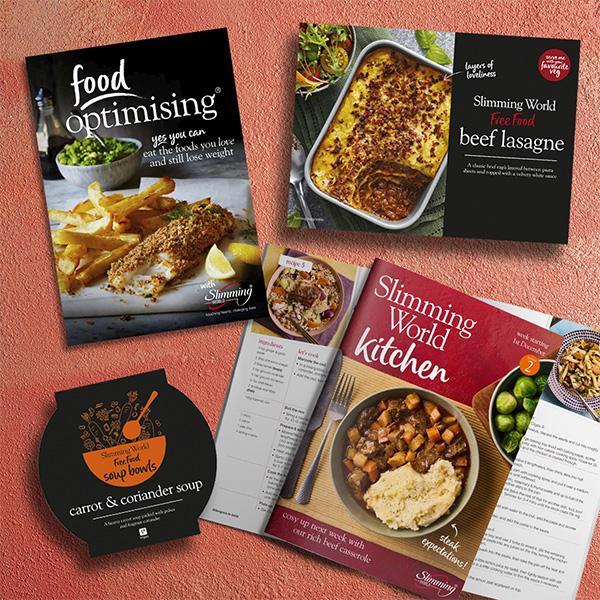 A Food Optimising book, Slimming World food range lasagne, Slimming World food range soup bowl and a Slimming World Kitchen Magazine displaying recipe instructions.